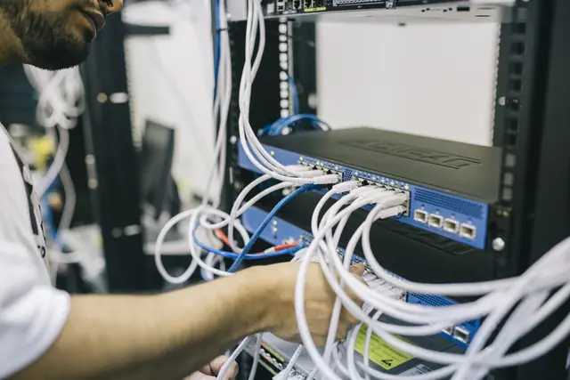 An engineer connecting network cables to a switch in a server rack